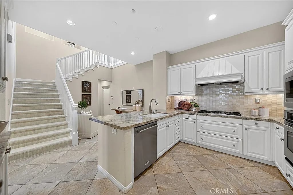 Kitchen with white cabinets, a granite island, and a carpeted staircase beside it.