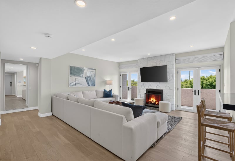 Living room with a white sectional, stone fireplace, and French doors to a tree-lined balcony.