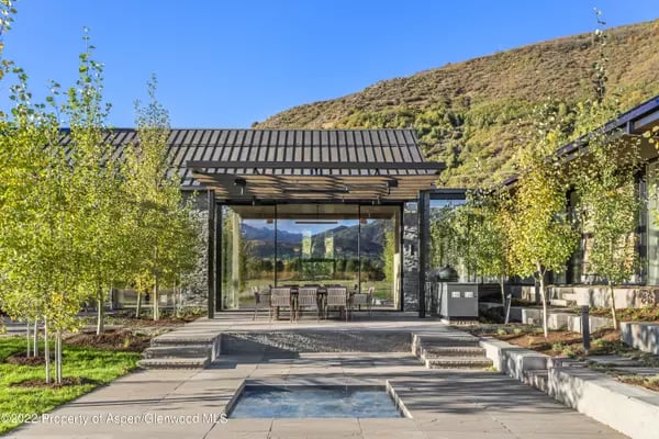 Modern mountain home with broad glass doors, a stone patio, and a reflecting pool.