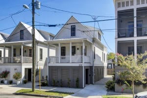 Two-story house with a covered porch and garage doors beside a taller neighboring building.