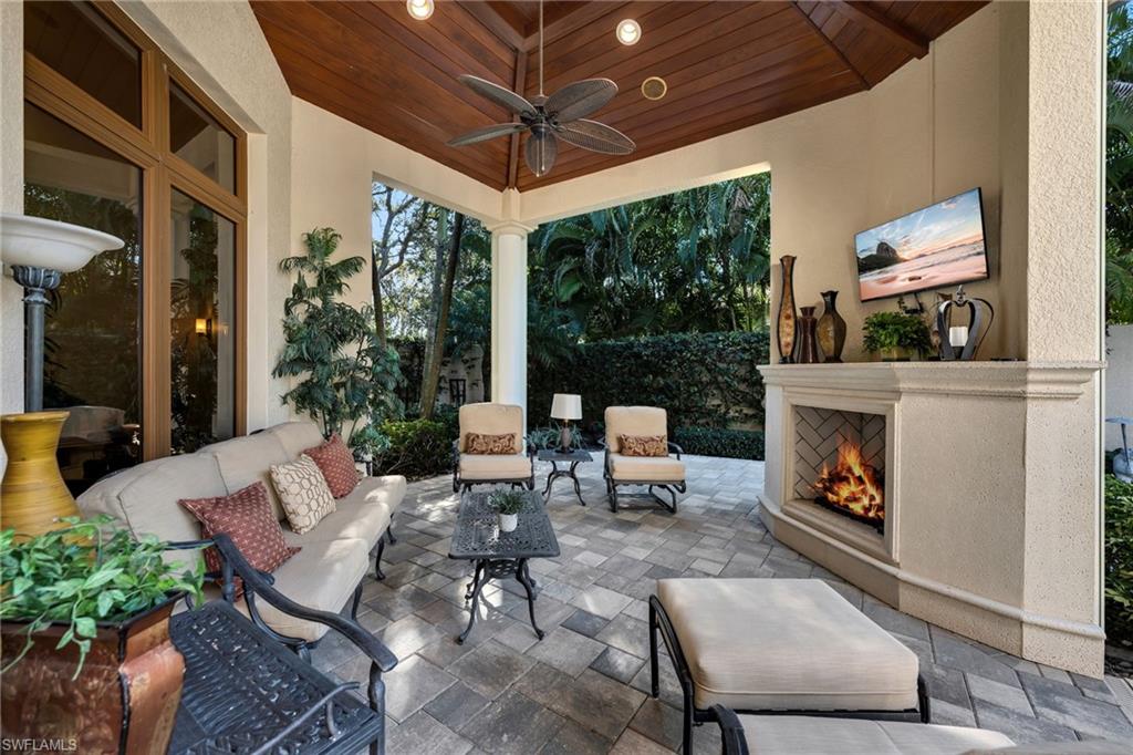 Luxury home in Quail West Naples featuring a covered outdoor living area with fireplace, vaulted wood ceiling and tropical landscaping.