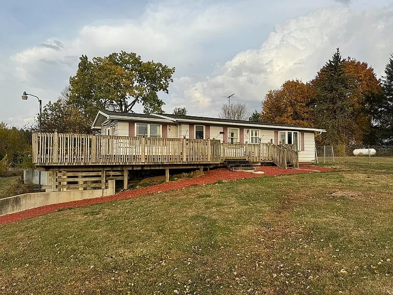 Single-story home with a raised wooden deck overlooking a sloping lawn.