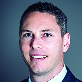 Man in a dark suit and white shirt with short dark hair.