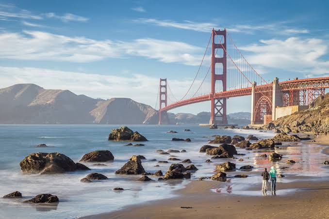 Golden Gate Bridge seen from rocky San Francisco beach with mountains in background