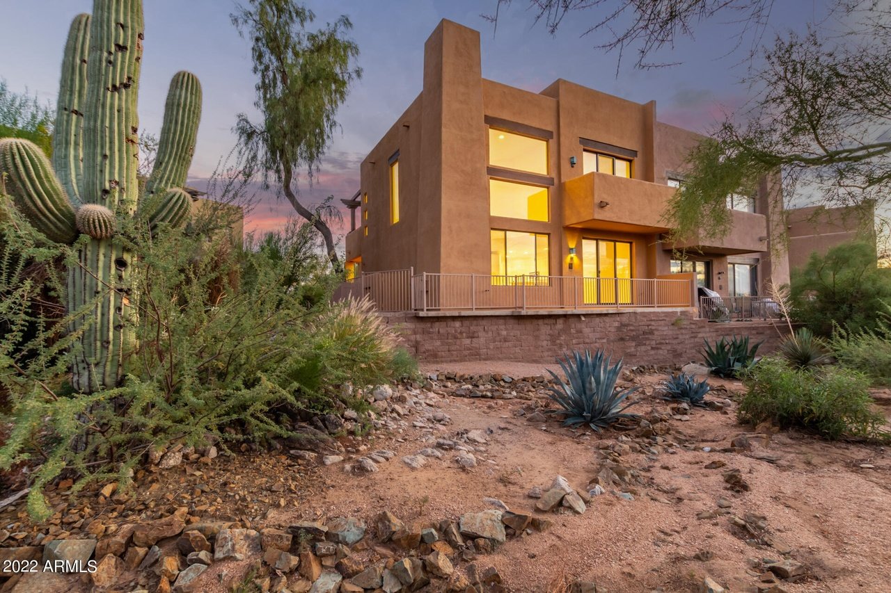 Modern two-story stucco home at dusk, surrounded by saguaros and desert landscaping.