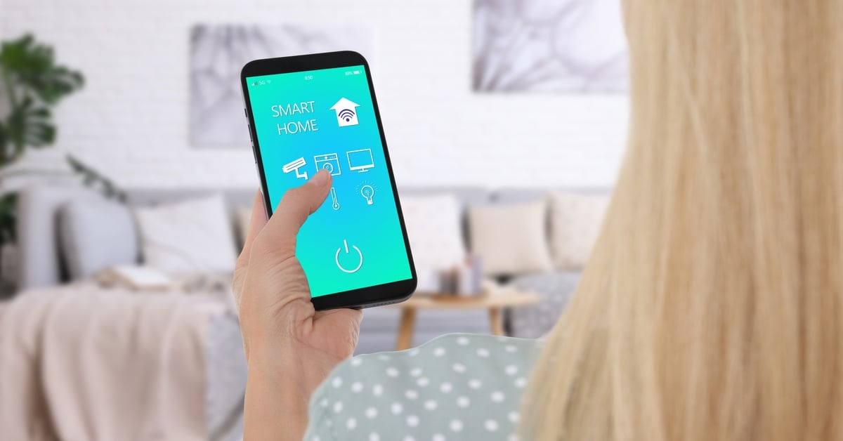 An over-the-shoulder view of a woman holding up a smartphone with 'Smart Home' on it with various apps and icons.