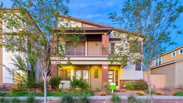 Two-story home with a covered balcony, brick accents, and desert landscaping.