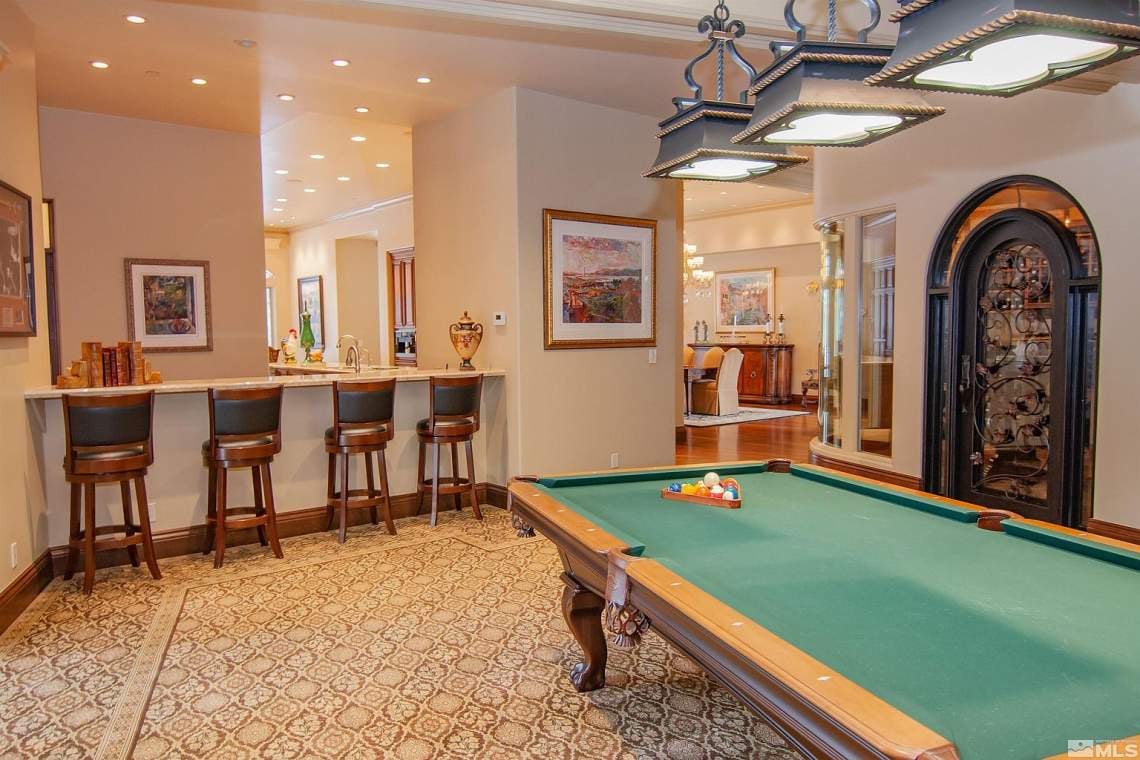 Game room with a green-felt pool table, bar seating, and an arched wine cellar.