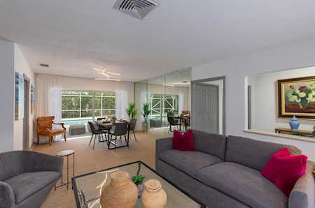 Living room with a gray sectional, pink cushions, mirrored wall panels, and a dining area by large windows.