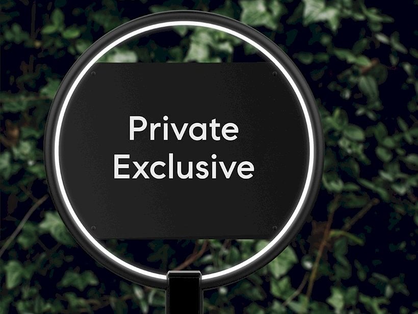 A modern black sign with illuminated circular framing displaying the words "Private Exclusive," set against a green leafy background, symbolizing the discretion and exclusivity of a Compass Private Exclusive real estate listing in Jackson Hole.