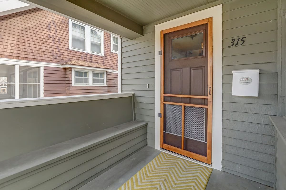 Covered front porch with a wood-framed screen door, gray siding, and house number 315.