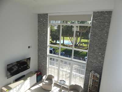 Double-height living room with tall windows, stone accents, and a view of the pool and lawn.