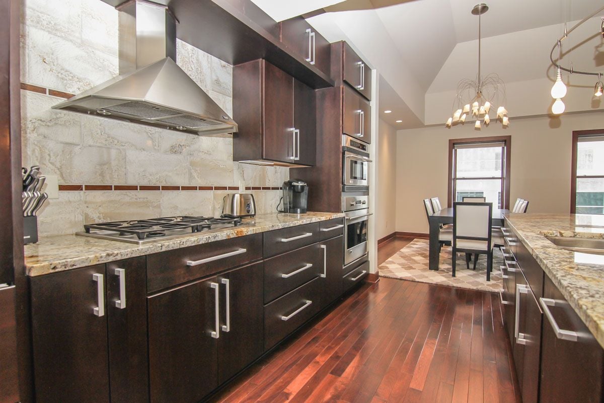 Modern kitchen with dark cabinetry, granite counters, stone backsplash, and an adjoining dining area.