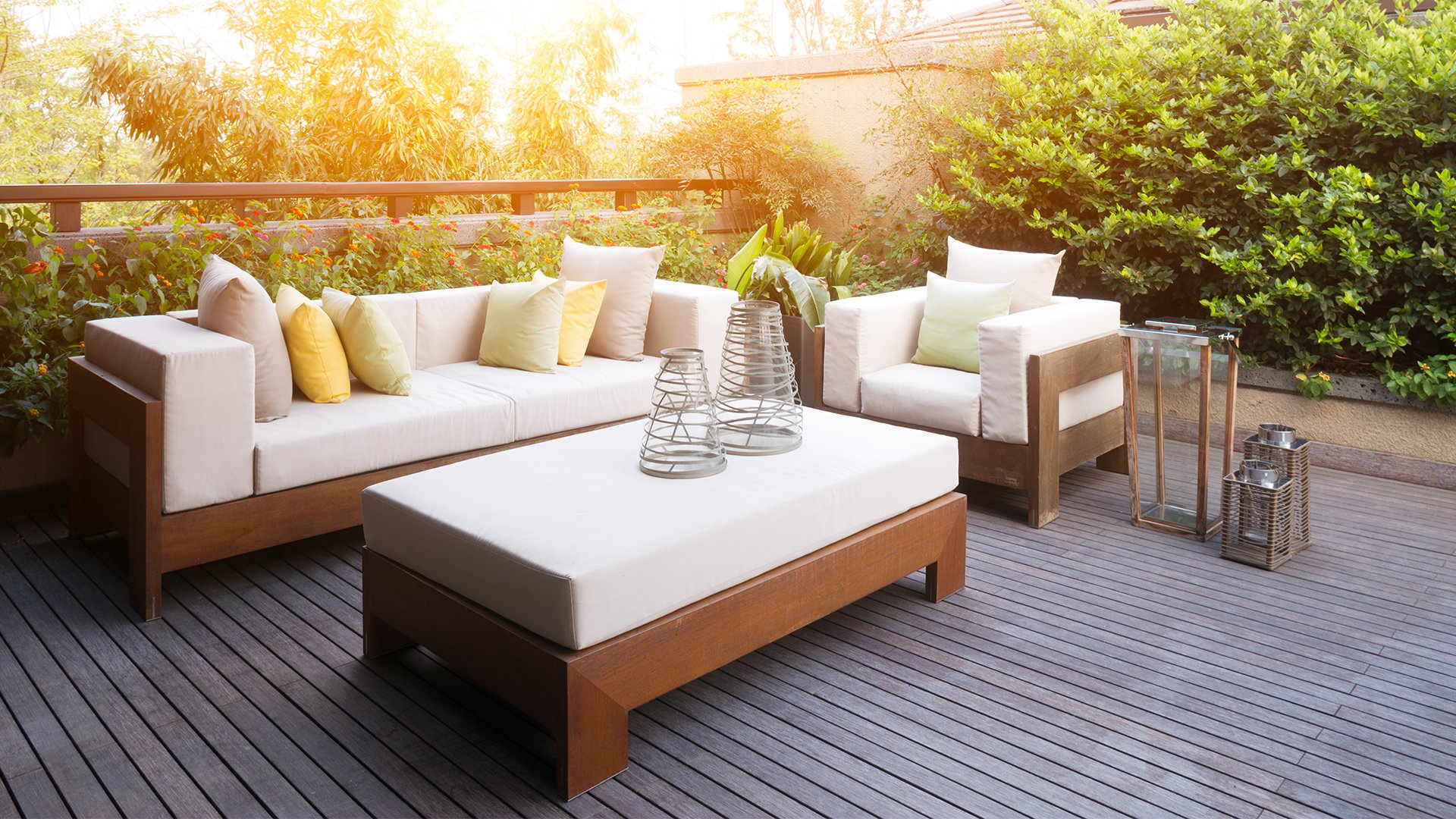 Outdoor patio with white-cushioned sofas, a low table, and dense greenery.