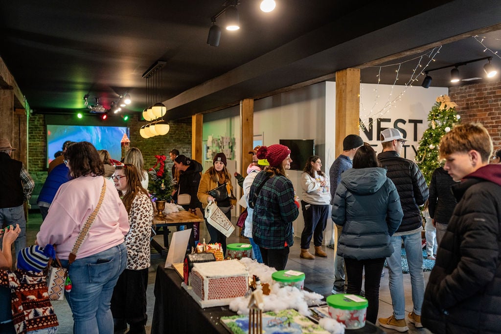 People mingle at a holiday gathering inside the Nest Realty office beside festive displays.