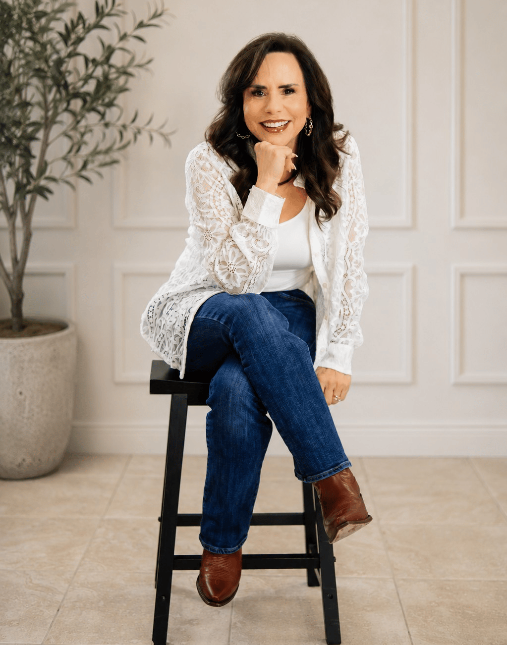 Cari Knowles seated on a stool, smiling in a white lace jacket and jeans.