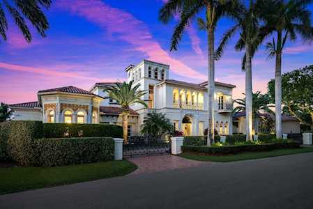 Mediterranean-style home with illuminated windows, palm trees, and manicured hedges at dusk.