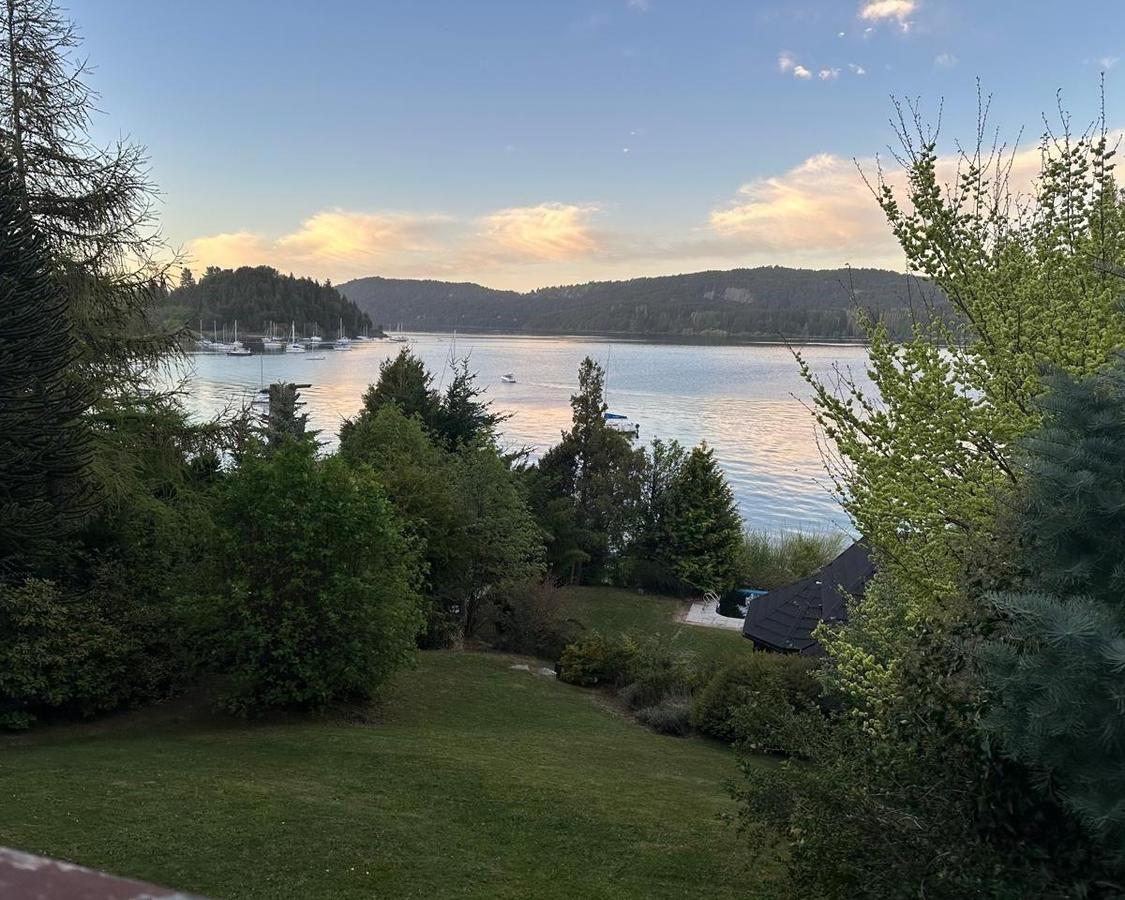 Waterfront garden overlooking a lake with sailboats and wooded hills at sunset.