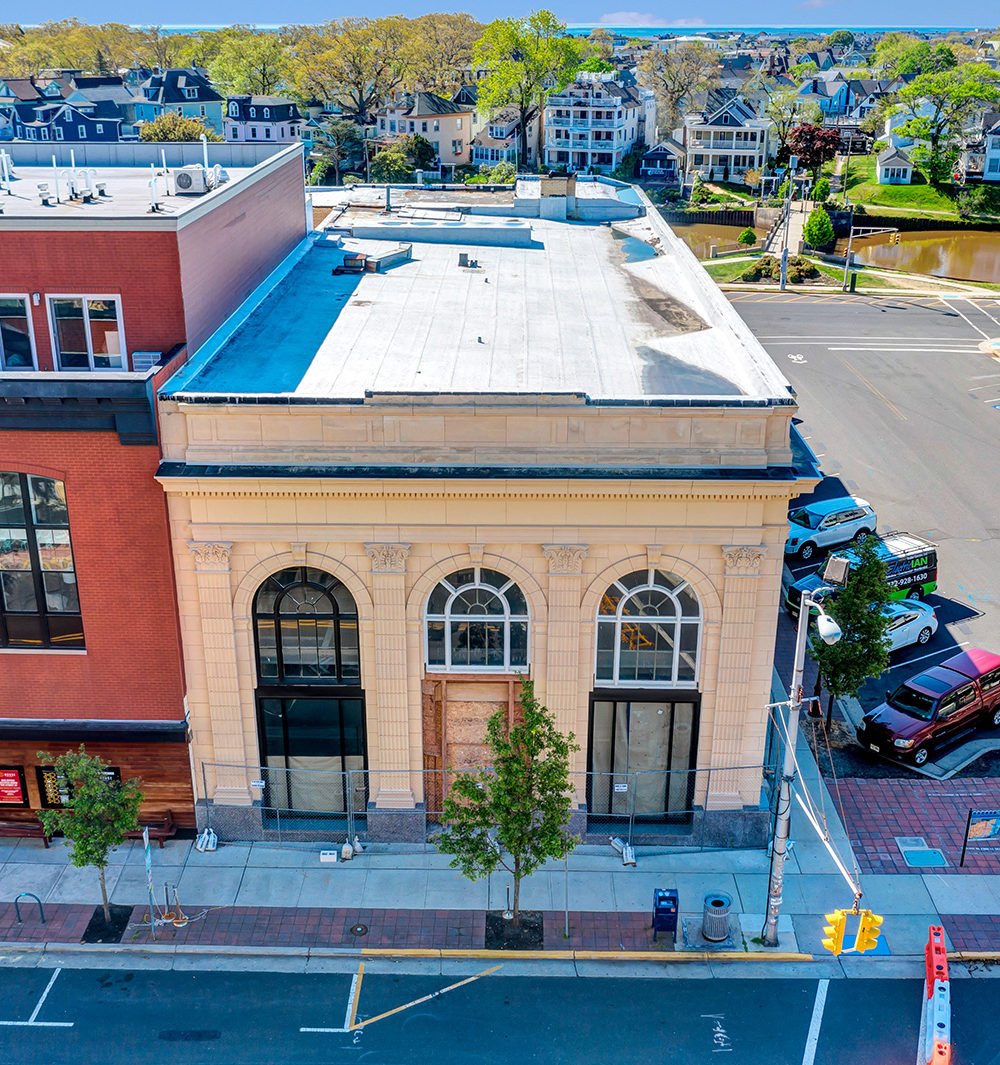 Street-corner building with a pale stone facade, arched windows, and sidewalk construction fencing.