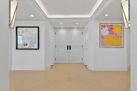 Condominium entry hall with white double doors, polished beige floor, and colorful wall art.