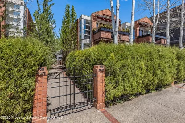 Modern residences with wood balconies behind a hedge and gated brick entrance.