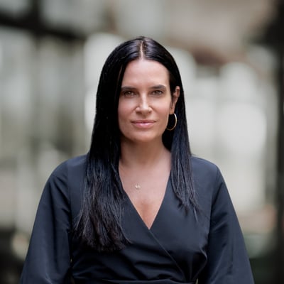 Amy Carlozzi wearing a dark wrap-style top and gold hoop earrings.