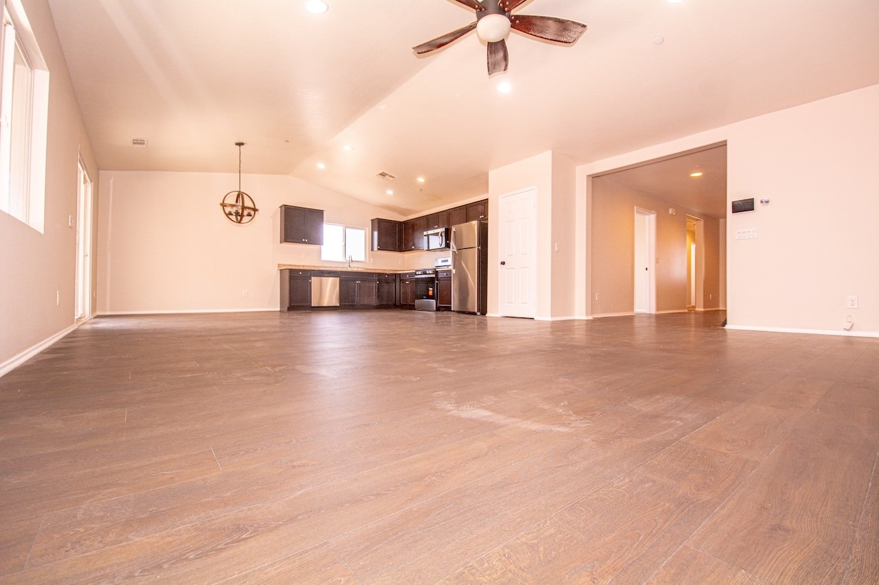Empty open-plan living area and kitchen with wood-look floors, dark cabinets, and stainless steel appliances.