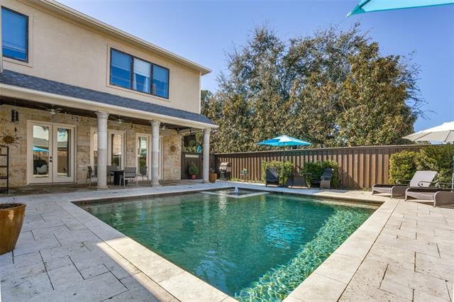 Backyard pool beside a two-story home, with patio seating and a fenced yard.