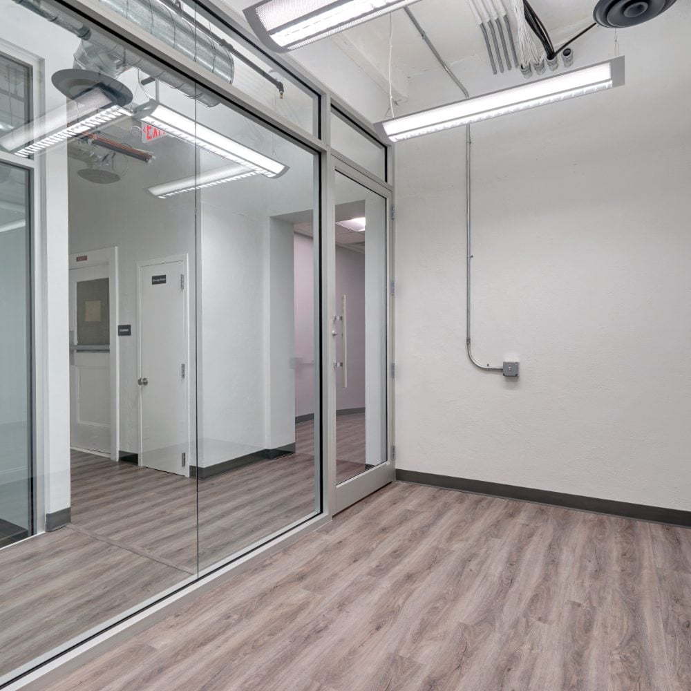 Vacant office with glass partitions and gray wood-look flooring.