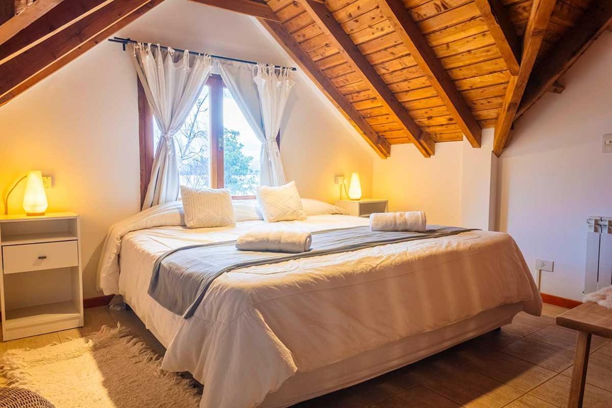 Hotel bedroom with a white bed, folded towels, and exposed wooden ceiling beams.