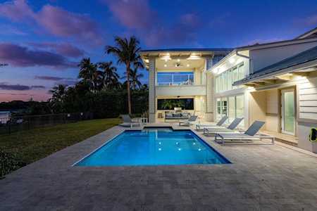 Illuminated swimming pool beside a modern two-story home, with lounge chairs on the patio at dusk.