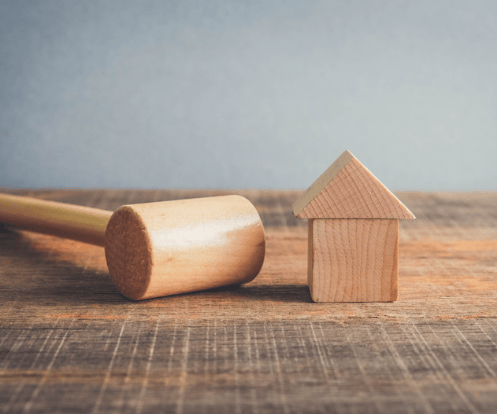 Wooden house model beside a wooden mallet on a weathered tabletop.
