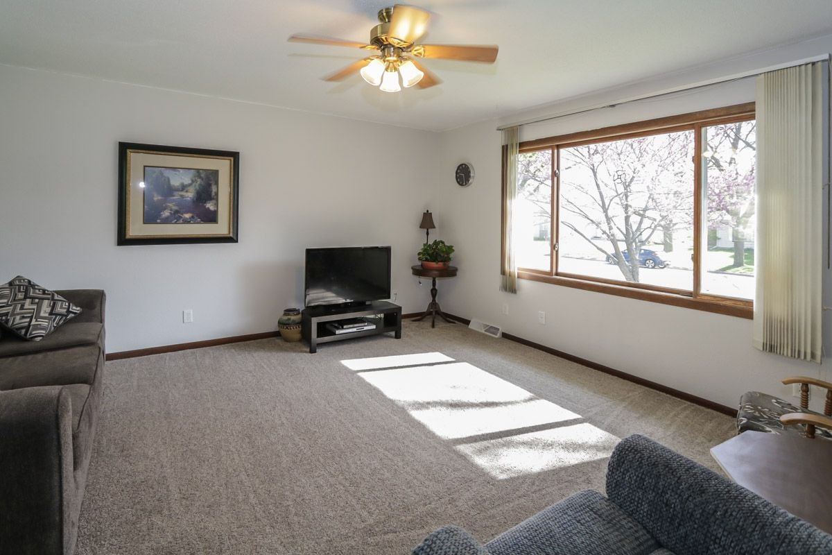 Living room with gray sofas, beige carpet, and a large sunny window overlooking flowering trees.