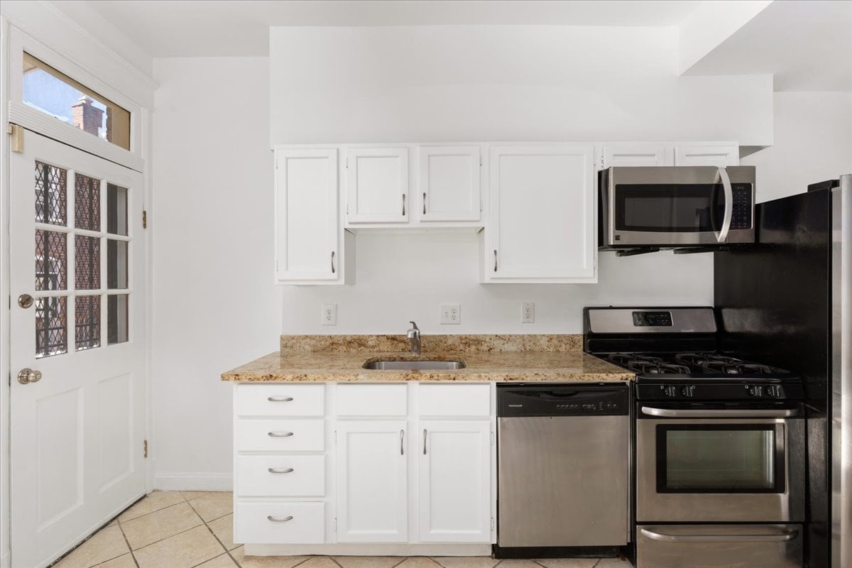 Kitchen with white cabinets, tan granite counters, stainless steel dishwasher, and black gas range.