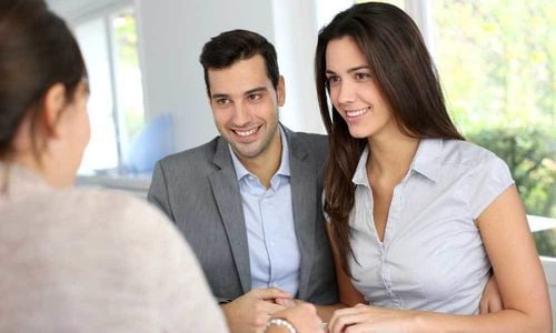 A smiling couple discusses paperwork with an agent in a bright office.