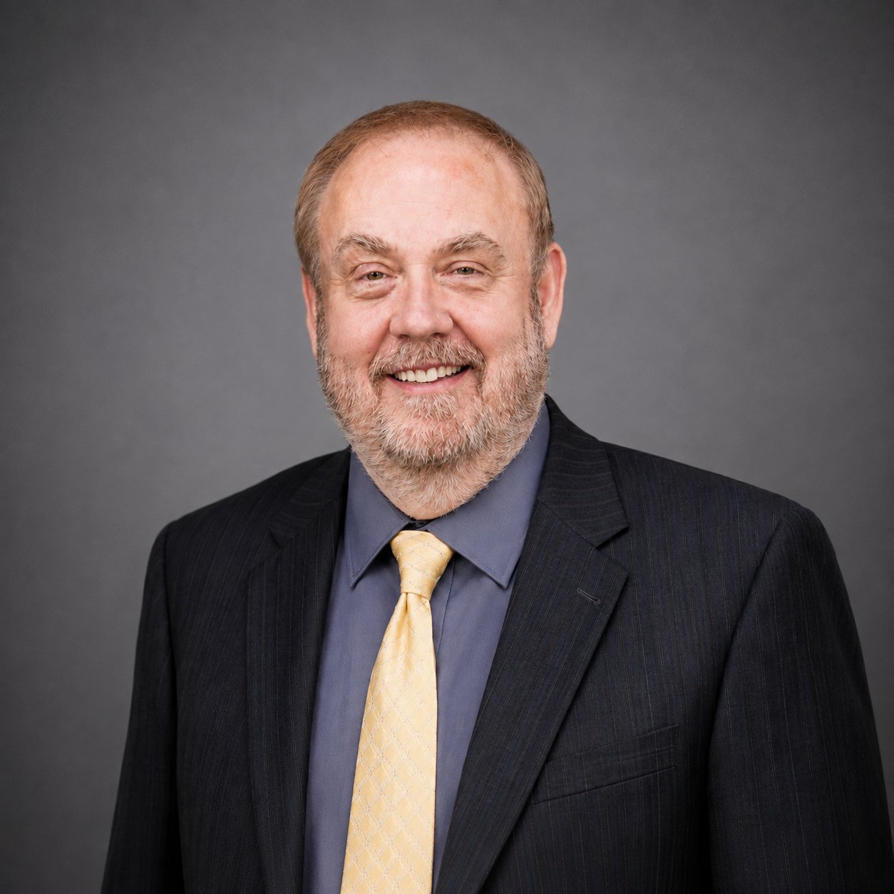 Mark Britton smiling in a dark pinstripe suit and pale yellow tie.