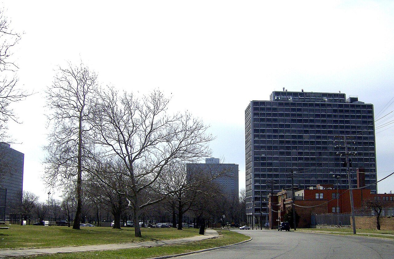 Detroit street curving past a grassy park and bare trees, with a dark office tower nearby.