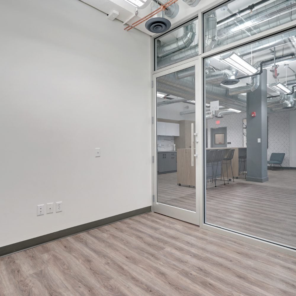 Office interior with glass partition, exposed ductwork, and kitchenette with bar seating.