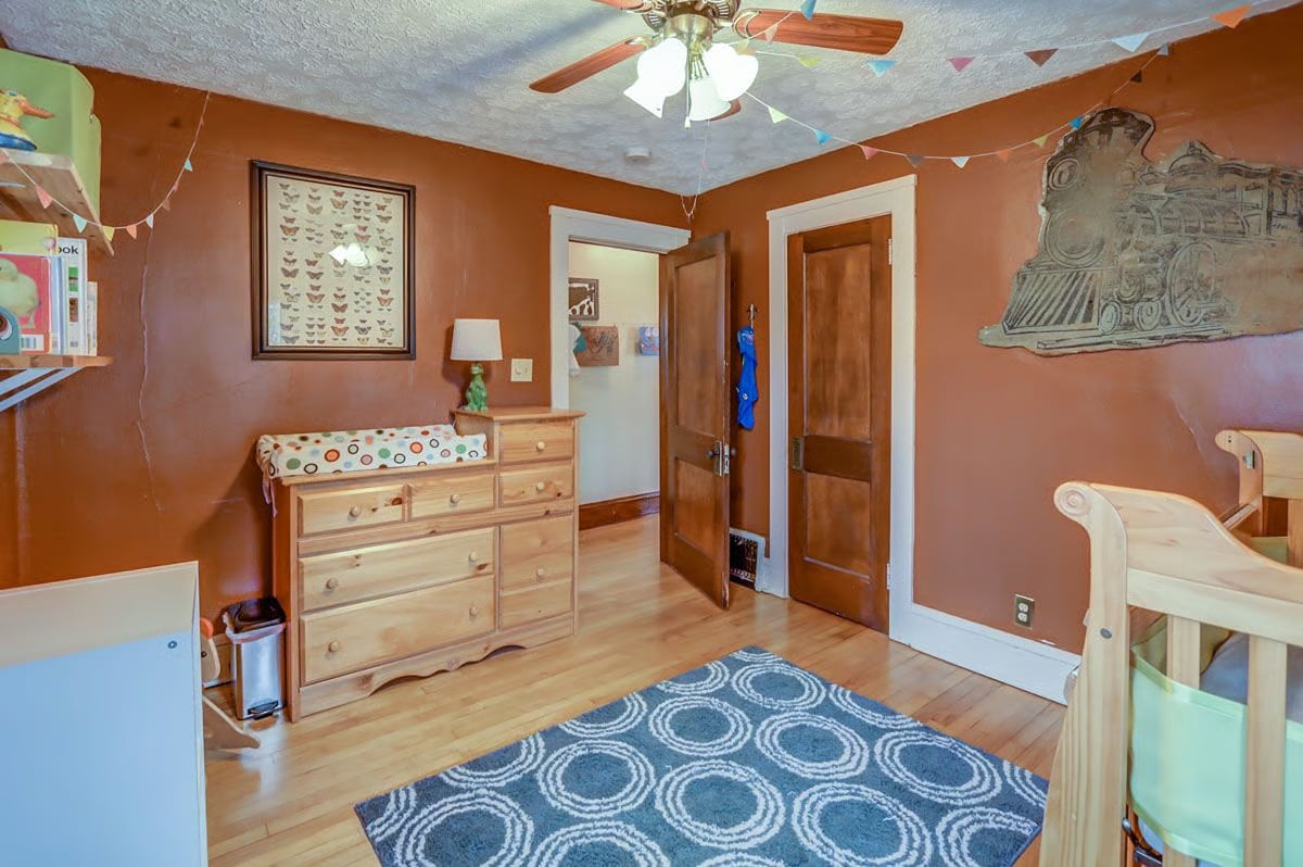 Nursery with rust-orange walls, a wooden dresser, crib, and blue patterned rug