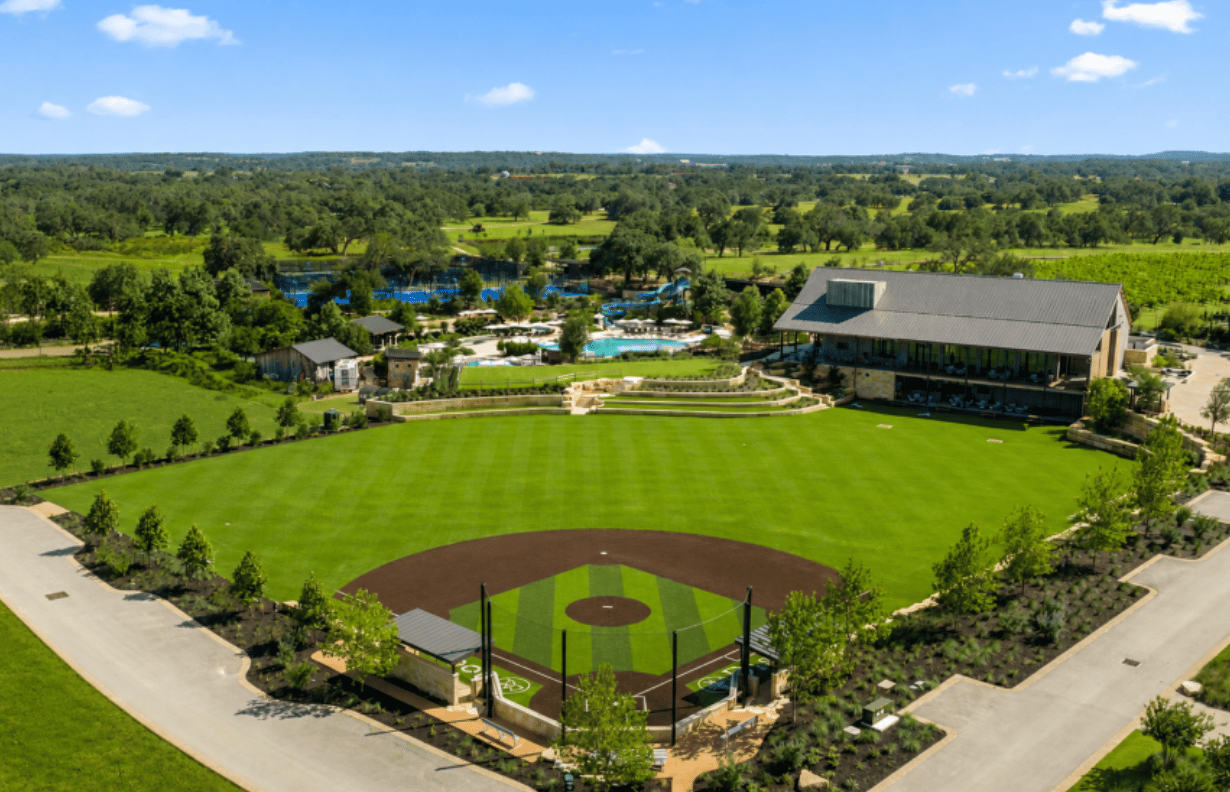 Driftwood Golf & Ranch Club grounds with a baseball field, clubhouse, pools, and wooded landscape.