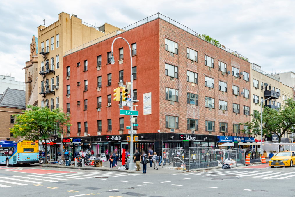 The Crossing condominium on the corner of First Avenue and East 14th Street, with red-brick upper floors and storefronts.