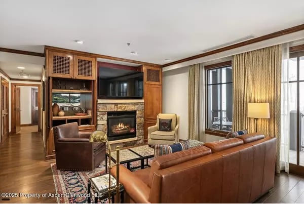 Living room with a stone fireplace, built-in wood cabinetry, leather seating, and tall curtained windows.
