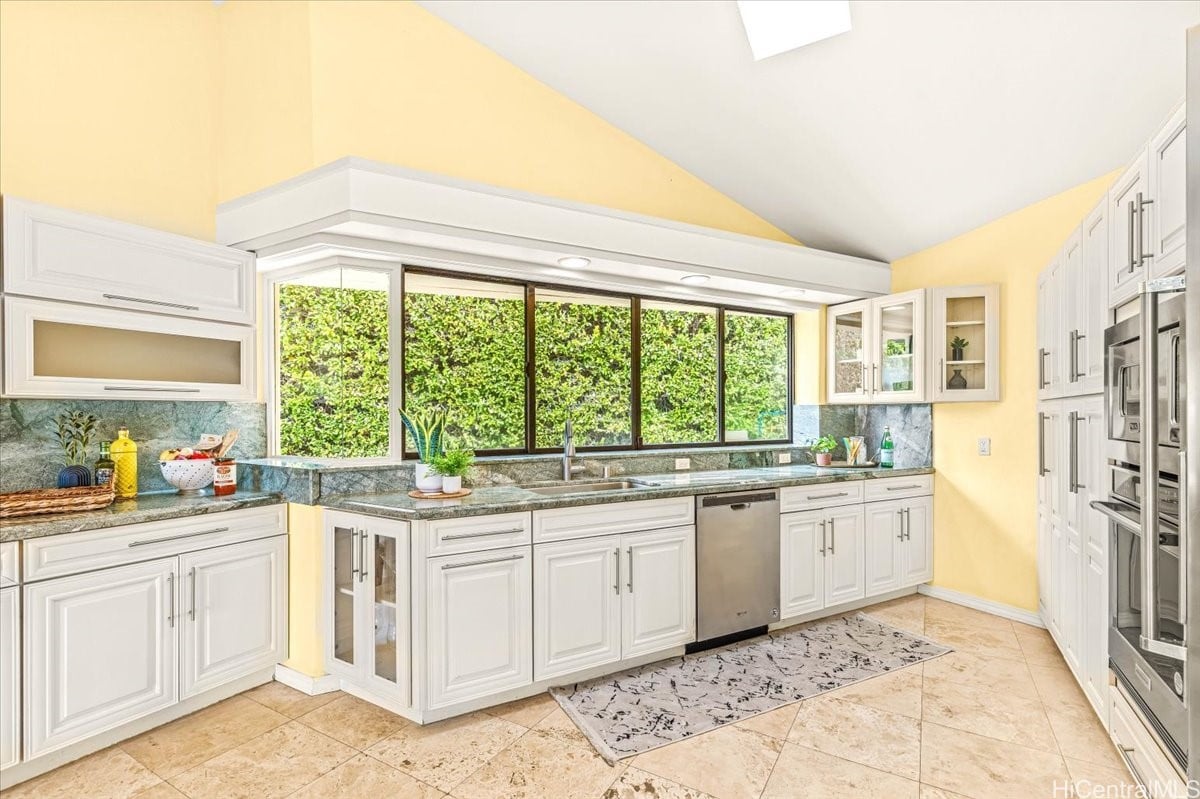 Bright kitchen with white cabinets, stone counters, and wide windows overlooking greenery.