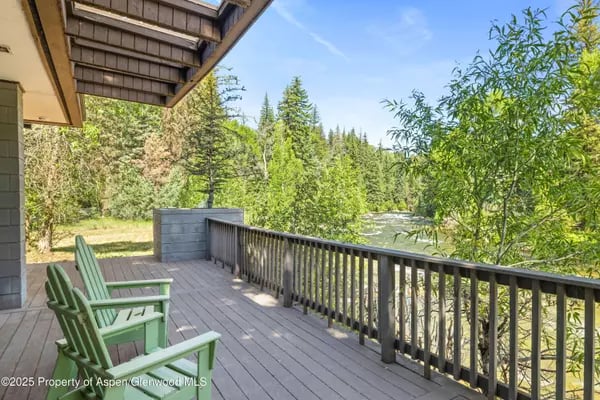 Wooden deck with green chairs overlooking a river and leafy trees.
