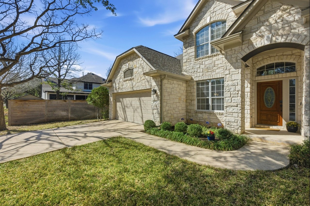 Two-story stone house with an attached garage, arched entry, and landscaped front garden.