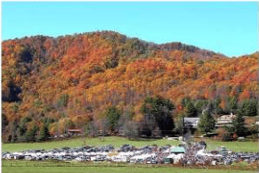 Autumn-colored mountain hills rise above a field of parked cars and small buildings.