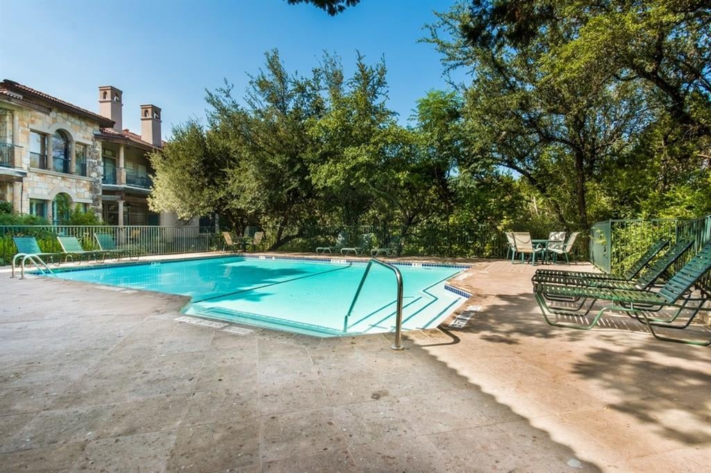 Community pool at Liberty Park Condominiums in West Lake Hills, Austin, with the complex's stone clubhouse building and shade trees in the background.