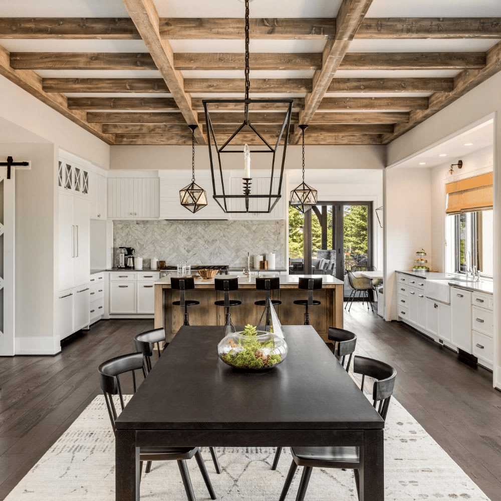 Kitchen and dining area with exposed timber ceiling beams, white cabinets, and a dark dining table.