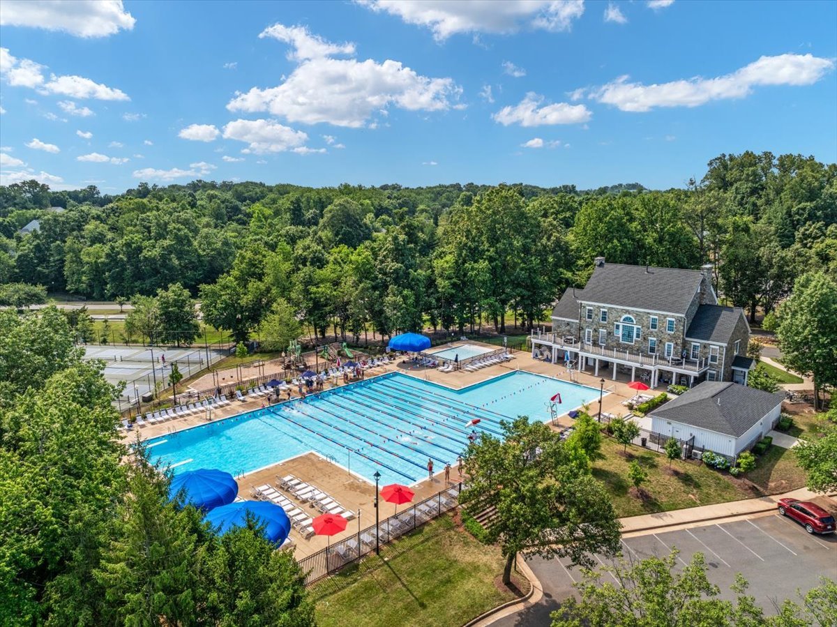 Aerial view of a community pool with lap lanes, lounge chairs, and a clubhouse amid mature trees.