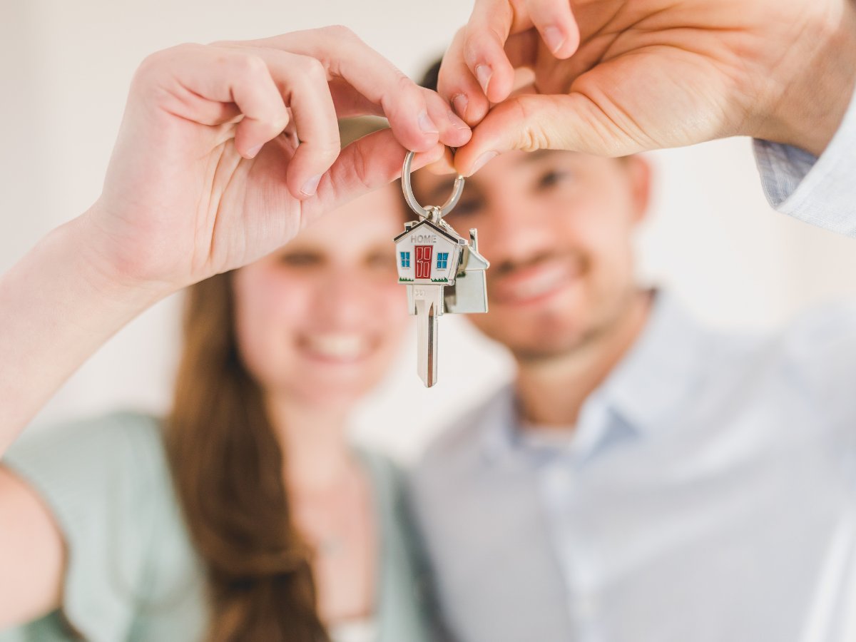 A couple holds house keys with a small house-shaped “HOME” keychain.